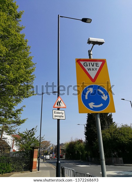 Road signs on the road to\
be careful of elderly people to cross the road and give way at the\
roundabout