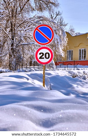 Road signs at the side of the road in the winter season; shrub and tree branches covered with a large layer of snow after a snowfall
