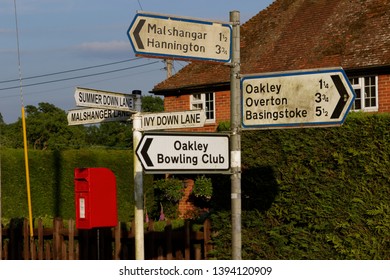 Road signs for villages from Malshanger with cottages and a red post box in the distance near Oakley Hampshire