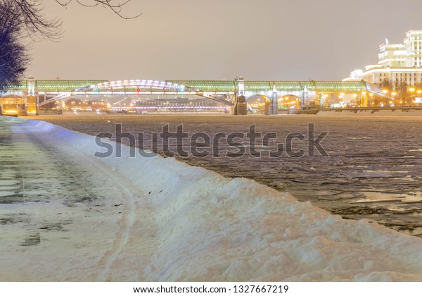 The road in the snow drifts near the river in the\
park in the evening