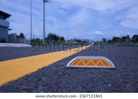 Road studs on the asphalt. Close up of reflective metal road studs being installed on the road beside yellow traffic lines on a background of trees and a sky with white clouds. Select focus