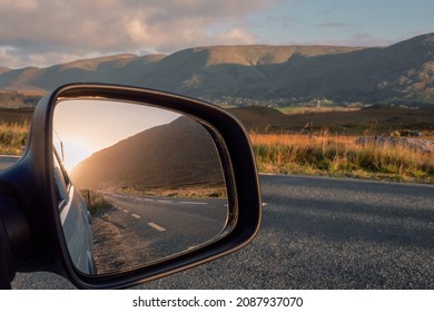 Road And Sun Rise View In A Car Mirror, Stunning Mountains Out Of Focus In The Background. Connemara, County Galway, Ireland. Car Travel And Tourism Concept.