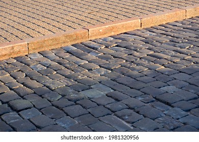 The Road Surface Paved With Traditional Dark Gray Granite Paving Stones. The Red Granite Curb Separates The Sidewalk From The Roadway.