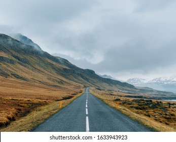 A road surrounded by rocks covered in greenery and snow under a cloudy sky and fog