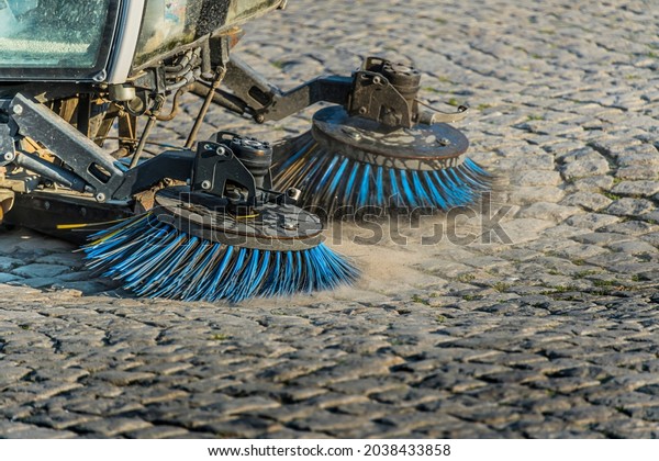 A road\
sweeping machine on a cobblestone\
street