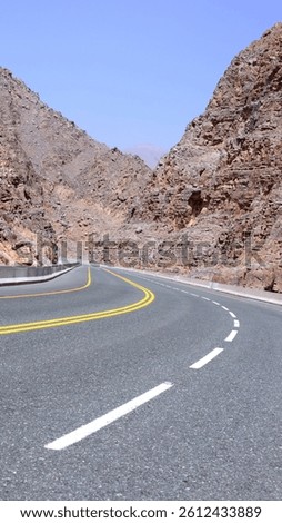 Road threads below leaning rock shelves, striped with mineral tension, each turn revealing twisted geometry, faded tones, and bold textures. Route of geological drama.