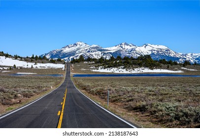 The road through the valley to the snow capped mountains. Mountain valley road landscape. Snowy mountain valley road way
