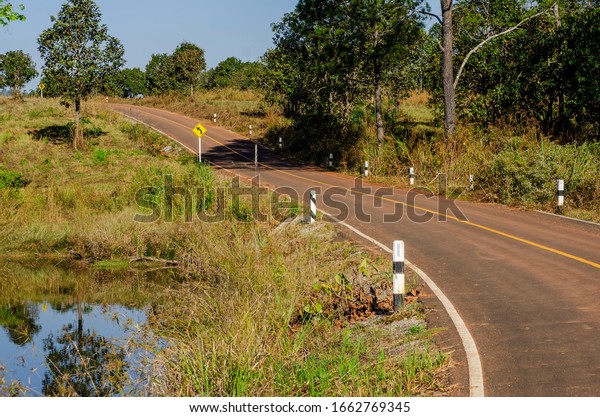 The road in the top bumped with green\
pastures and puddles on the side of the\
road.