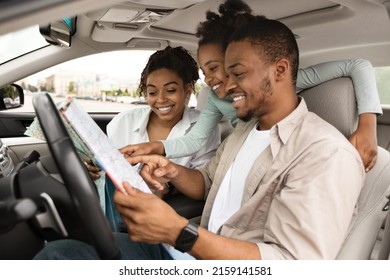 Road Trip Adventure. Happy African American Family Holding Map Sitting In Car Choosing Destination For Vacation. Travel By Automobile. Transportation And Navigation. Selective Focus, Side View