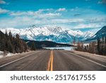 Road trip with car driving on highway road with snow covered rocky mountains in winter at Kootenay plains area, Alberta, Canada