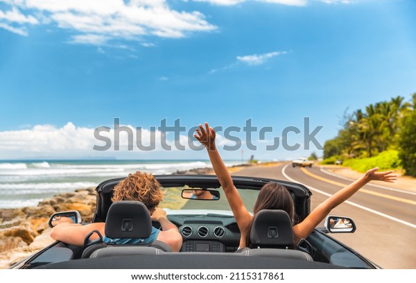 Road trip car holiday happy couple driving\
convertible car on summer travel Hawaii vacation. Woman with arms\
up having fun, young man\
driver