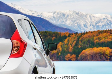 Road Trip Concept, Car Driving Travel In Fall And Autumn Season, Lake, Beautiful Foliage And Mountains Covered By Snow As Background