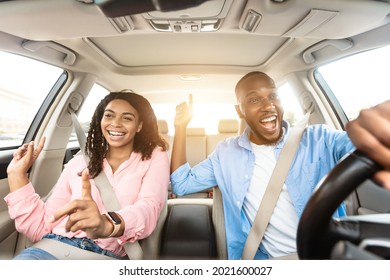 Road Trip Concept. Front View Portrait Of Excited Playful African American Couple Driving Luxury Car, Dancing To Music And Singing Favorite Song, Resting On Weekend Going On Vacation, Sun Flare