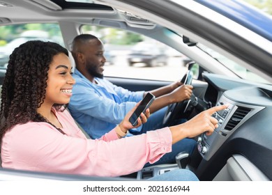 Road Trip Concept. Profile Side View Portrait Of Smiling Black Couple Sitting In Luxury Car, Man Driving Auto, Woman With Mobile Phone Pointing At The Road, Showing Way, Using Digital Map Application