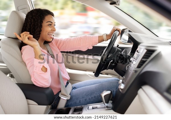 Road Trip Concept. Profile side view portrait of\
excited playful black woman driving luxury car, dancing to music\
and singing favorite song, resting on weekend going on vacation or\
home from work