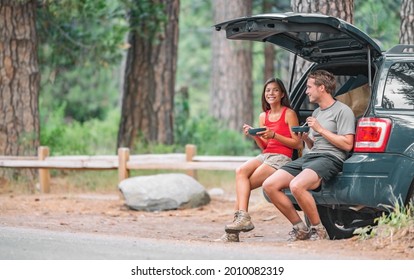 Road trip couple tourist eating food lunch at back of car on summer camping vacation travel. Happy driving people.