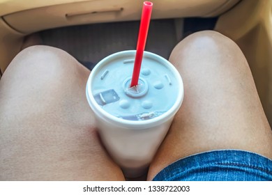 Road Trip - Legs In Blue Jean Shorts With To Go Take Out Throw Away Styrofoam Cup With Straw Held Between Them In Car - Close-up And Selective Focus