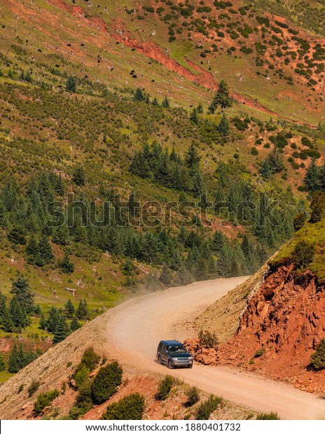 Road trip in the mountains: a solitary SUV on a\
mountain dirt road with no protection and subject to rock\
landslides, just after a bend in the\
road