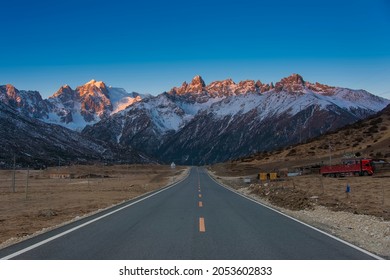 A road trip on a highway in Tibet. The highway passing high snowcapped mountain peaks and golden yellow autumn foliage.