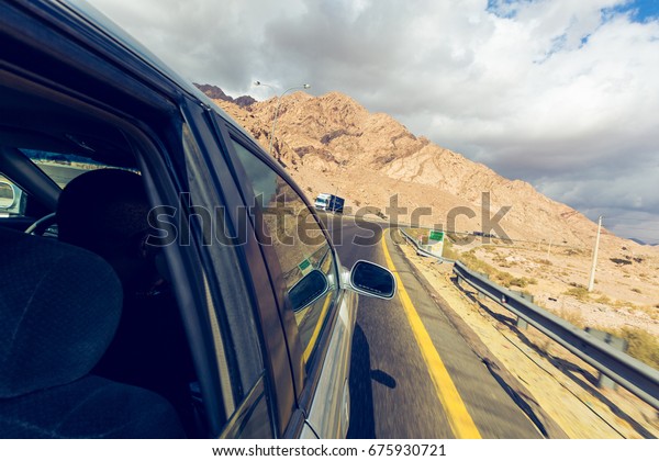 A road trip point of view of a road and car on a\
highway desert, point of view from someone hanging out of a window.\
Travel is freedom.