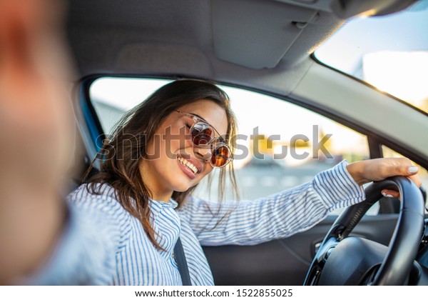 Road trip selfie. Young woman using her\
smartphone and making selfie while driving a car. Young woman\
taking selfie picture with smart phone camera in car. Smiling young\
woman taking selfie\
picture