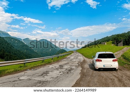 Road trip in spring with a white german compact car across bumpy roads with picturesque mountain panoramas of the Julian Alps near Spodnja Sorica Železniki in Slovenia
