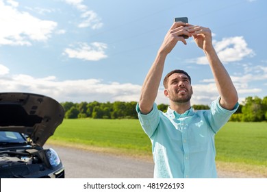 Road Trip, Transport, Travel, Technology And People Concept - Young Man With Smartphone Catching Signal And Open Hood Of Broken Car At Countryside