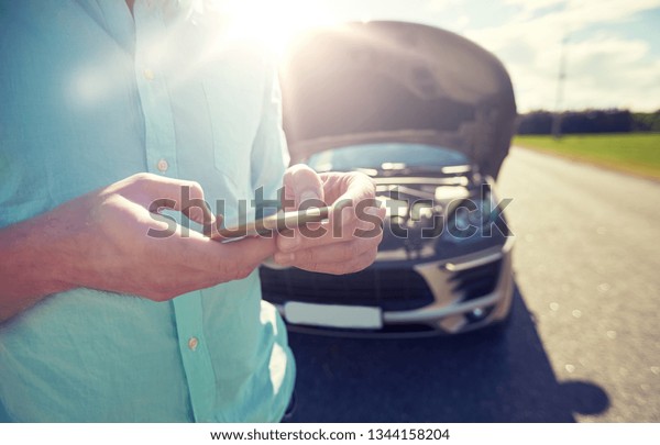 road trip,\
transport, travel, technology and people concept - close up of man\
with smartphone and broken\
car