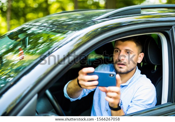 road trip, transport, travel, technology and
people concept - happy smiling man with smartphone driving in car
and taking selfie