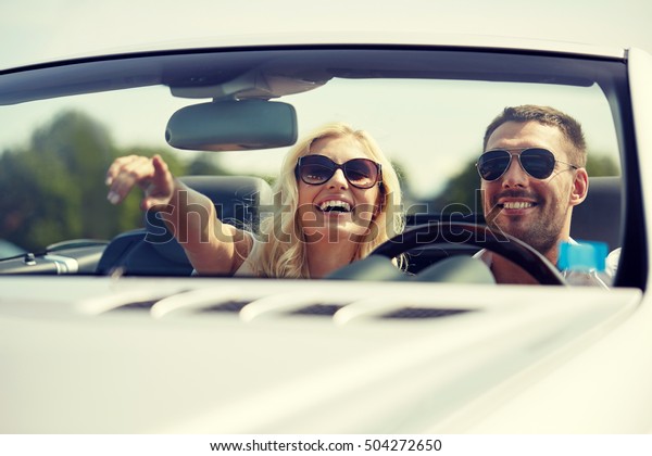 road trip, travel,\
couple and people concept - happy man and woman driving in\
cabriolet car outdoors