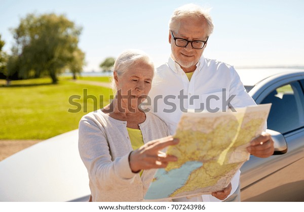 road trip, travel and old\
people concept - senior couple at car looking for location on map\
in summer