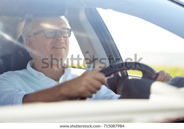 road trip, travel and old people concept -\
happy senior man in glasses driving\
car