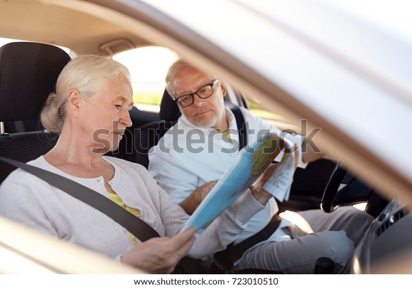 road trip, travel and old people concept -\
happy senior couple with map driving in\
car