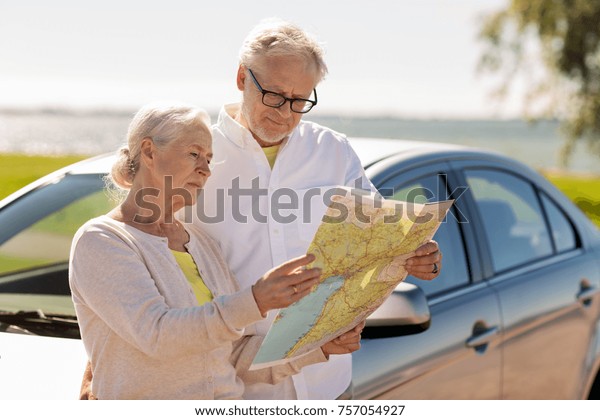 road trip, travel\
and old people concept - senior couple with car looking for\
location on map in summer