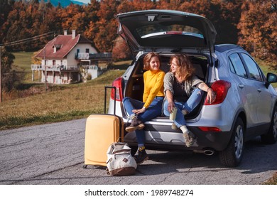 Road Trip -  Two Teenager Smiling Girls Sitting In The Boot. Travel By Car
