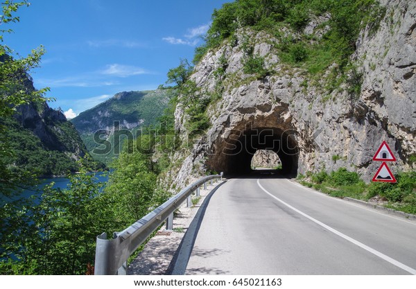 Road tunnel in the rock. Highway tunnel\
cutting through a mountain. Empty road. Nature and travel.\
Montenegro, Lake Piva. Near border with\
Bosnia