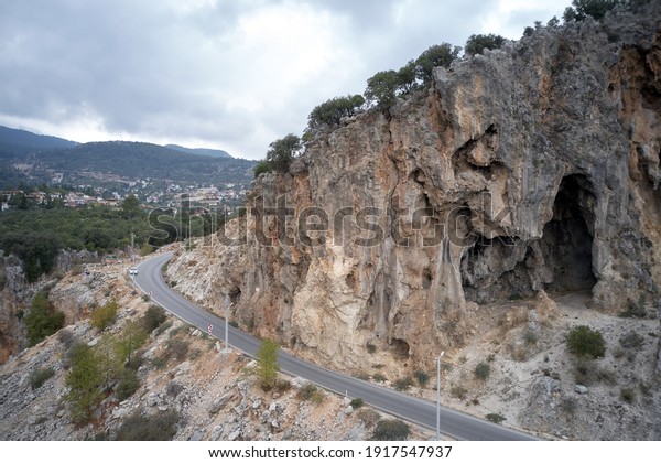 Road under high cliff\
in the mountains. Aerial view of rocky mountain cliff beside\
highway asphalt road.
