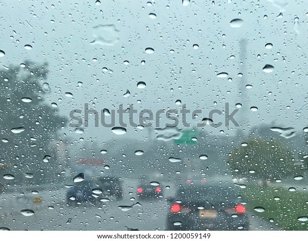 Road view\
through car window blurry with heavy rain.Driving in rain\
weather.Raindrops on the windscreen to\
car.
