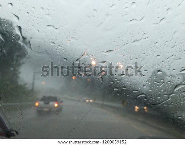 Road view\
through car window blurry with heavy rain.Driving in rain\
weather.Raindrops on the windscreen to\
car.
