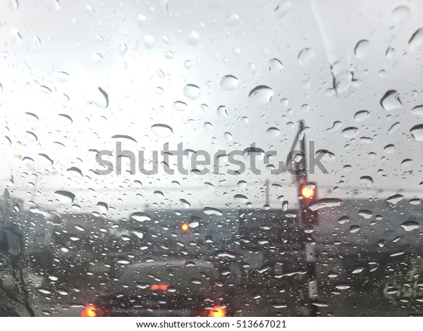 Road view through car window with rain drops, Driving in\
a heavy rain. A traffic in the heavy rain,View through the window\
and Shallow depth of field composition. Traffic light under raining\
dark   