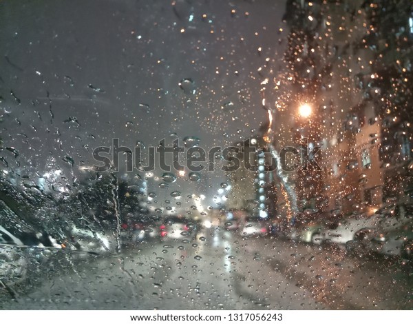 Road view through car windshield with blurry and\
bokeh heavy rain drops, concept of driving in rain that is bad\
driving conditions. -\
Image