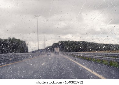 Road view through windshield car window with going rain drops during driving at speed. Unfocused highway. Autumn