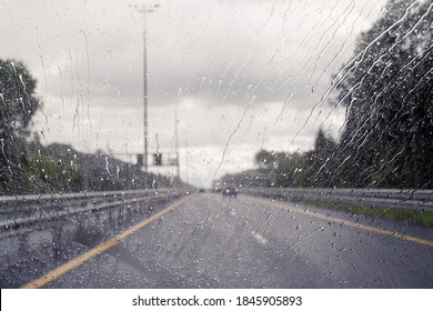 Road view through windshield car window with going rain drops during driving at speed. Unfocused highway. Autumn