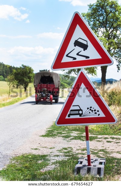 Road warning sign on slippery\
road. Spilled gravel on the road. Country road in the Czech\
Republic
