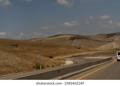 A road with a white van driving down it. The road is empty and the sky is clear