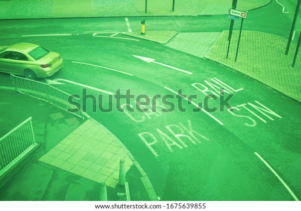 Road with white written\
indications for car park or train station in bright green tone from\
the footbridge panel of Queensgate Shopping Centre in\
Peterborough.