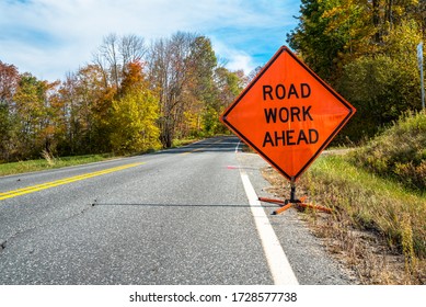 Road Work Ahead Road Sign Telling Motorists To Be Alert As They Are Entering A Contruction Area On A Country Road On A Sunny Autumn Day. Beautiful Fall Colors.