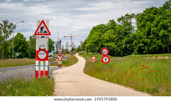 Road work sign under construction. Cars not\
allowed. Caution and safety symbol. Red and white triangle safety\
sign beside the path.