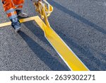 Road worker applying yellow road markings to asphalt using stencil tape. Close-up of a road worker applying yellow paint to asphalt with stencil tape