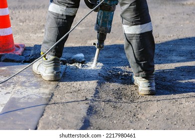 A Road Worker Breaks Asphalt With An Impact Jackhammer At A Construction Site. Noisy Drill. Road Construction Works.